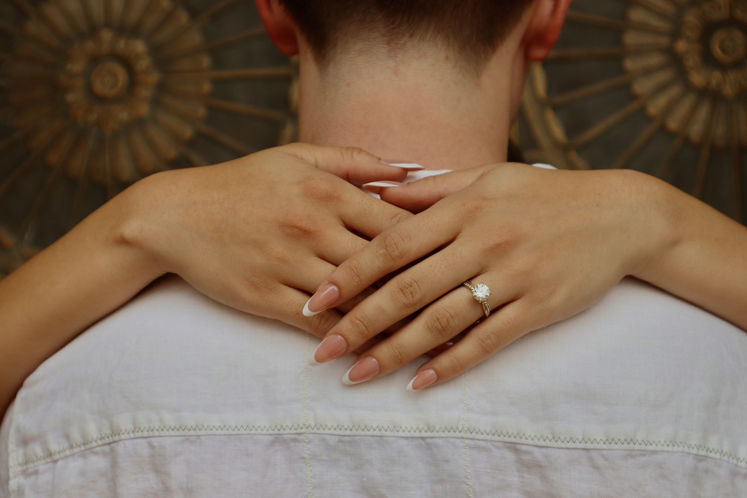 Hands clasped behind his neck, engagement ring visible
